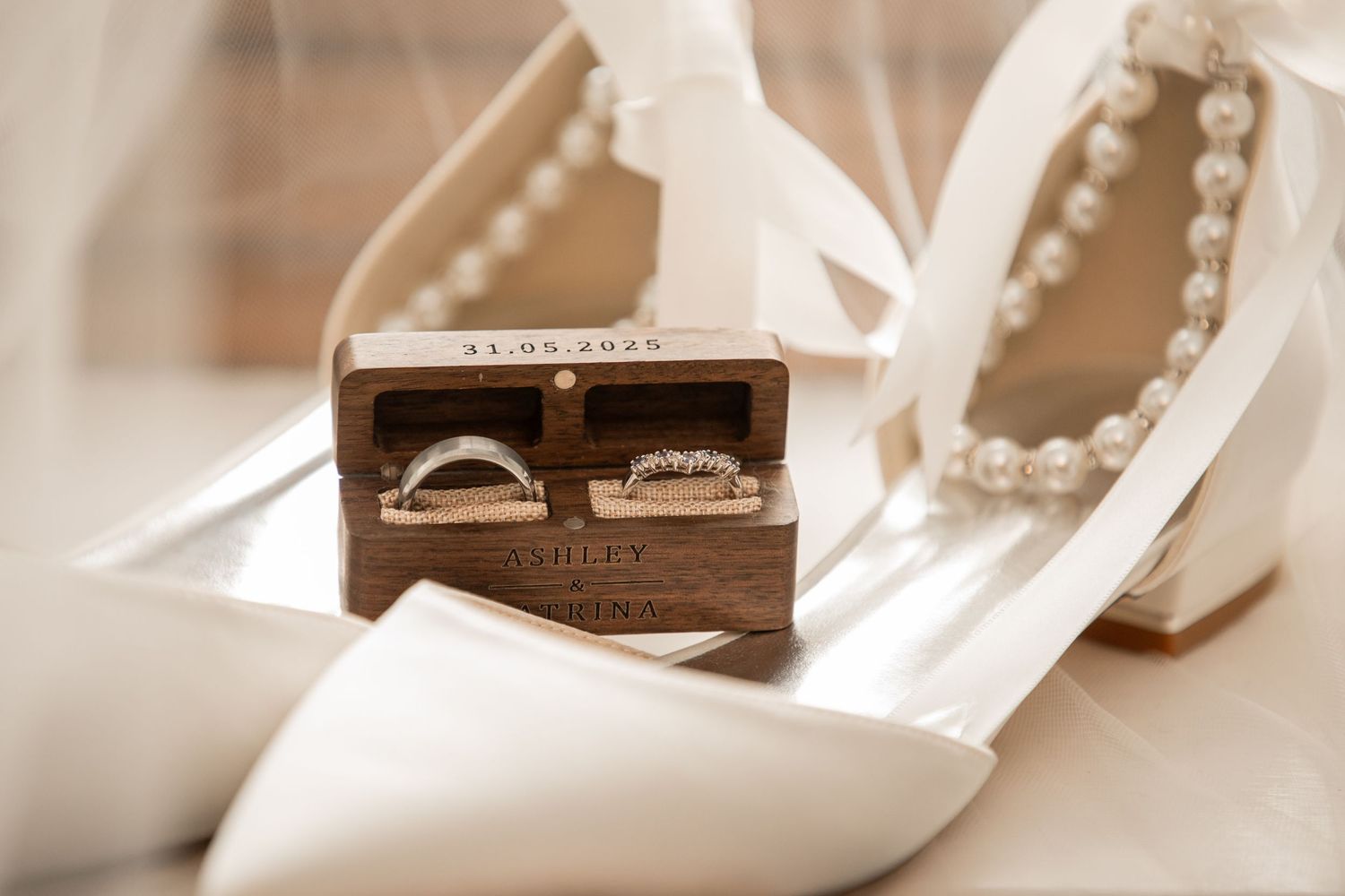 Wedding rings in wooden box placed on white bridal shoes.