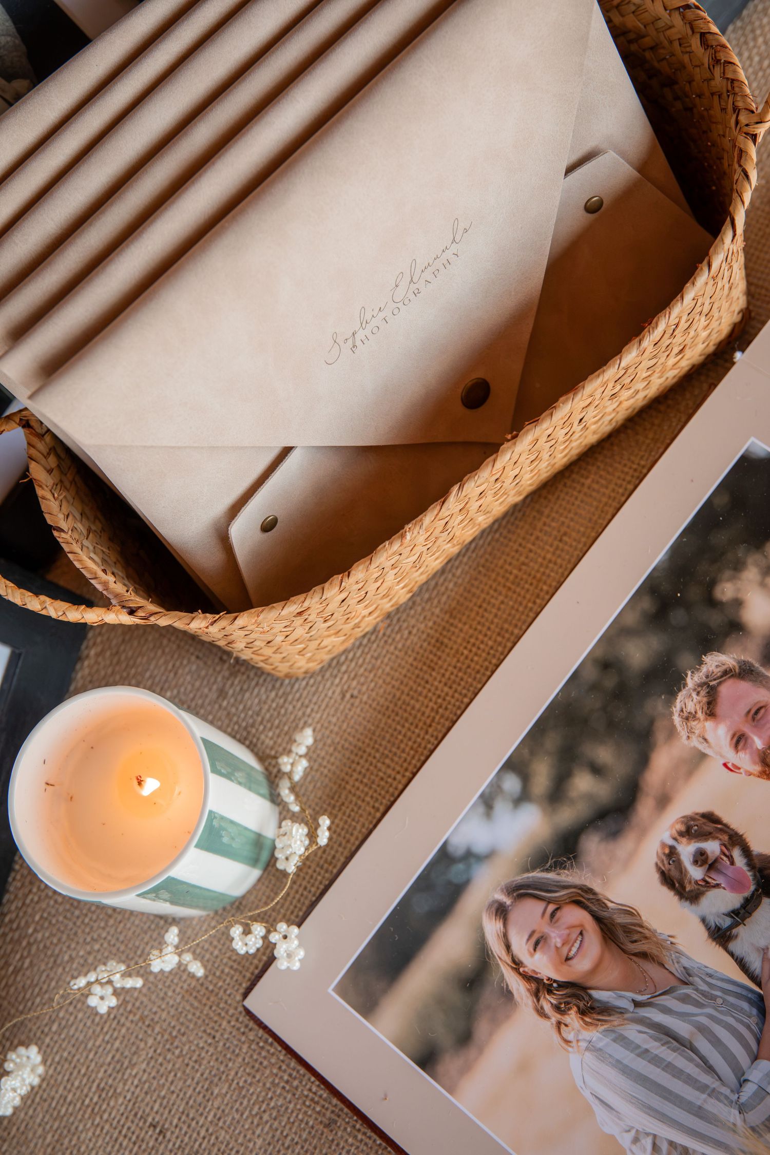 A wicker basket with a leather envelope, lit candle, and framed family photo on a textured surface.