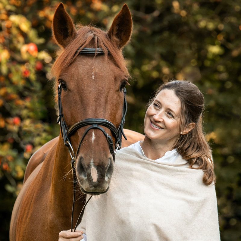 Horse and handler sharing a tender moment against autumn foliage background.