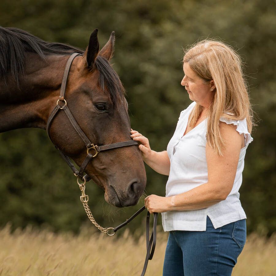 A woman in white interacts affectionately with a brown horse against a natural background.