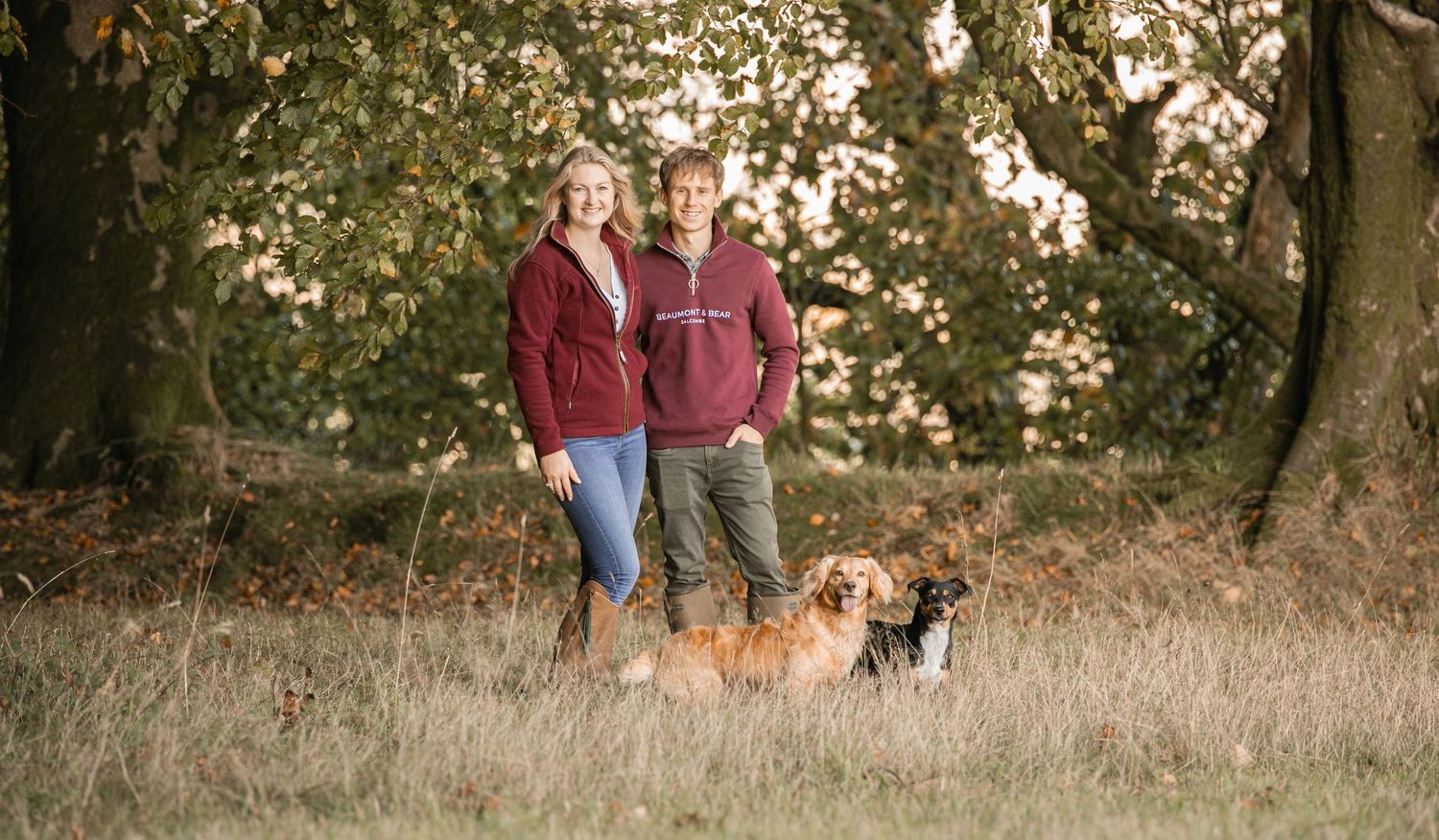 Autumn portrait of a couple with their dogs in a wooded park setting.