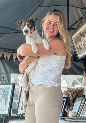 A person in a white top holding and cuddling with a gray and white dog in what appears to be a vehicle interior.