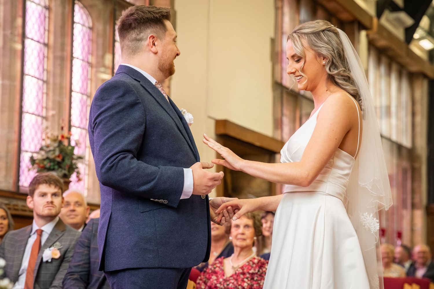 Bride and groom exchanging vows at a church wedding ceremony, with guests seated in the background.