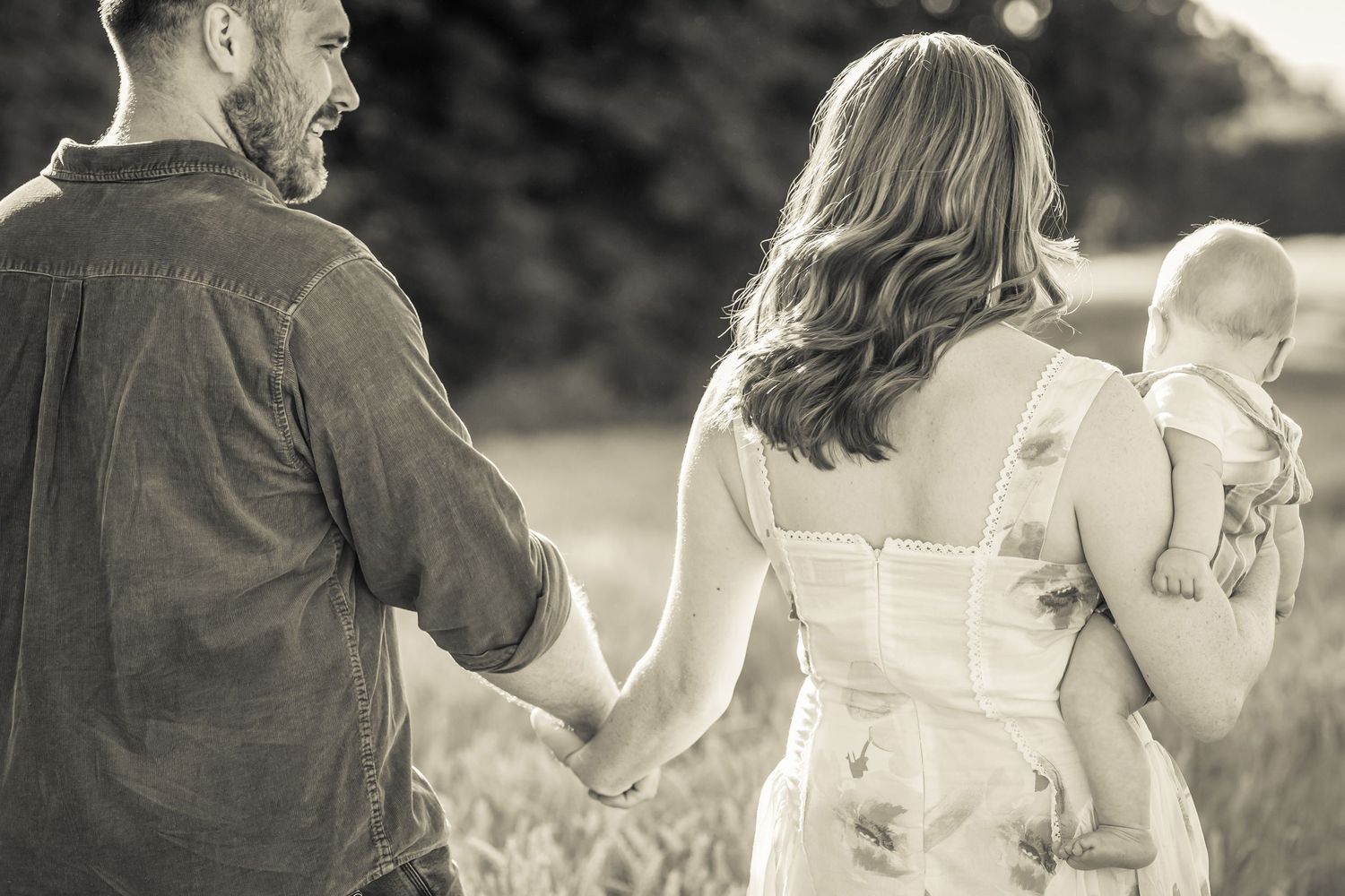 Romantic couple walking in field during golden hour family photography session with Sophie Edmunds Photography in the Cotswolds.
