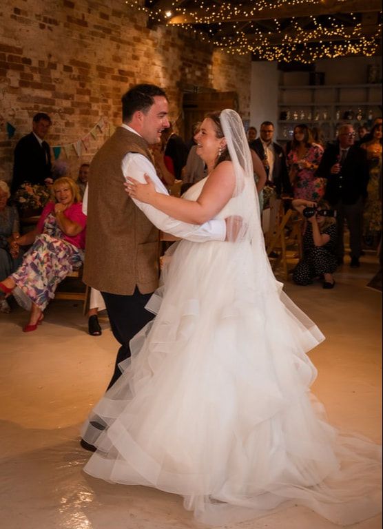 Couple dances together in a rustic brick venue decorated with twinkling lights during their first wedding dance.