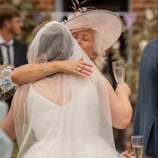 A bride in a white wedding dress holds a champagne glass during an outdoor celebration at a brick venue.