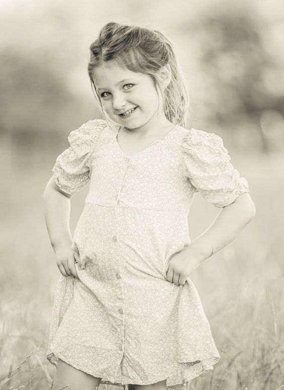 A series of sepia-toned photographs showing a young child in a white lace dress playing outdoors in a dreamy setting.