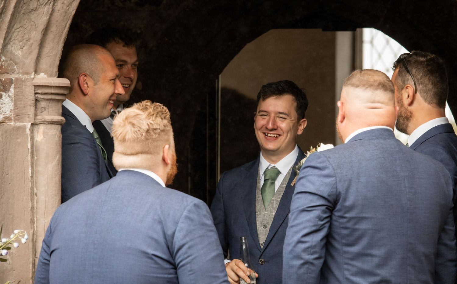 A group of people in formal business attire gather in conversation at an indoor event or meeting space.