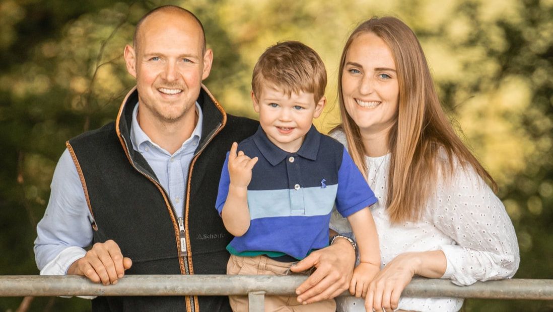 A family poses together outdoors during a fall photo session with warm golden lighting and natural scenery.