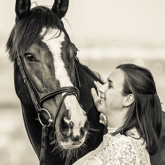 A tender moment between a dark horse and a person with long hair against a light background.