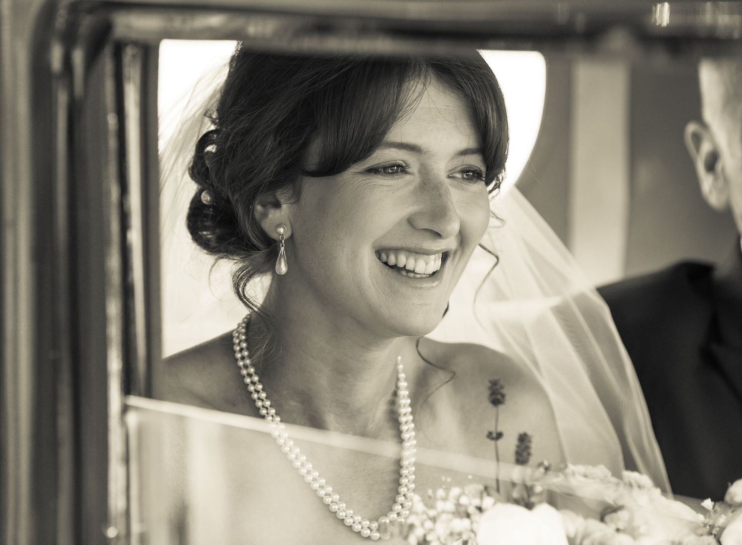 Elegant bride wearing pearl necklace and veil in vintage car in Caerphilly in Wales.