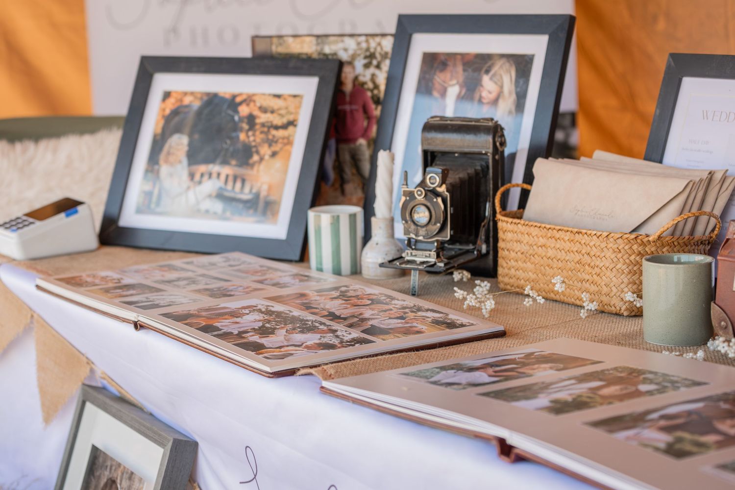 Vintage photo display table with open album, antique camera, framed photos, and decorative items at an outdoor event.