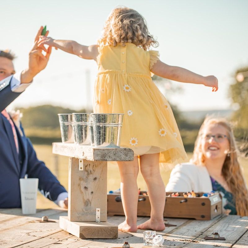 A child in a yellow dress dances on an outdoor table during a sunny gathering with refreshments.