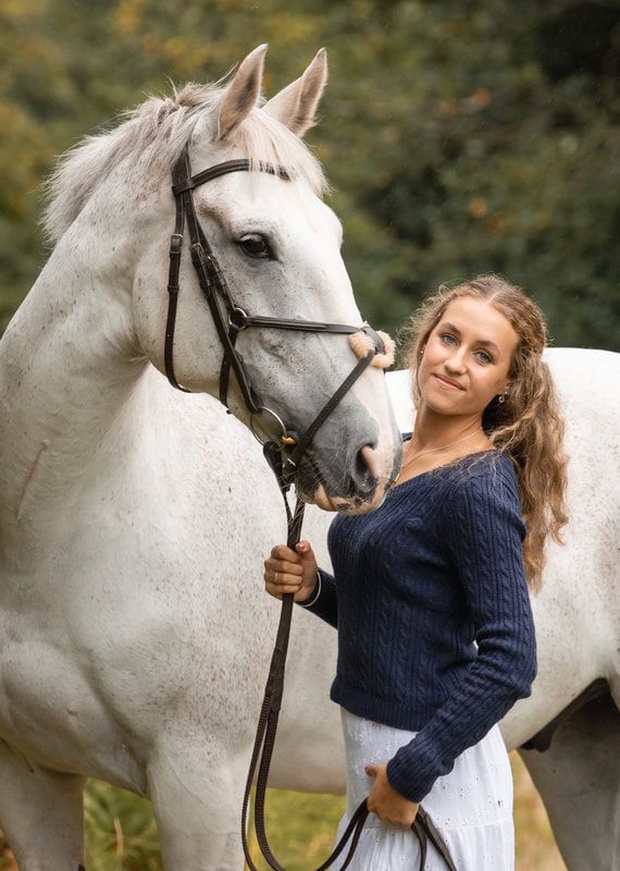 A white horse and person in a navy sweater share tender moments in an outdoor setting.
