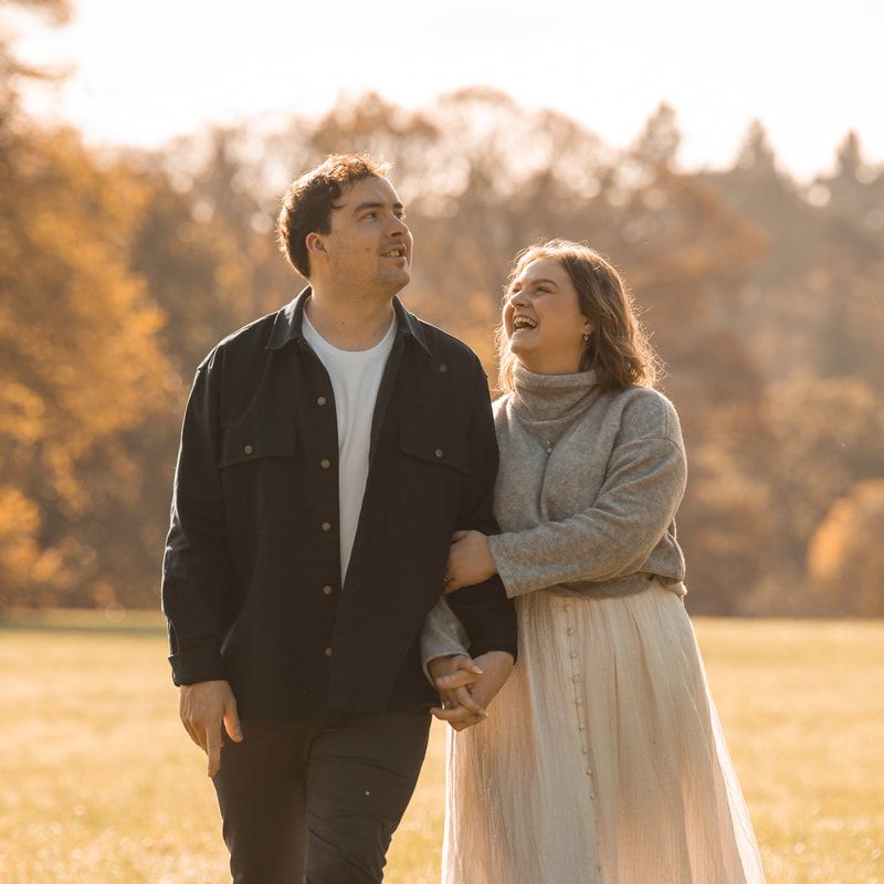 A couple laughs together while walking through a sunlit autumn field in warm golden light.