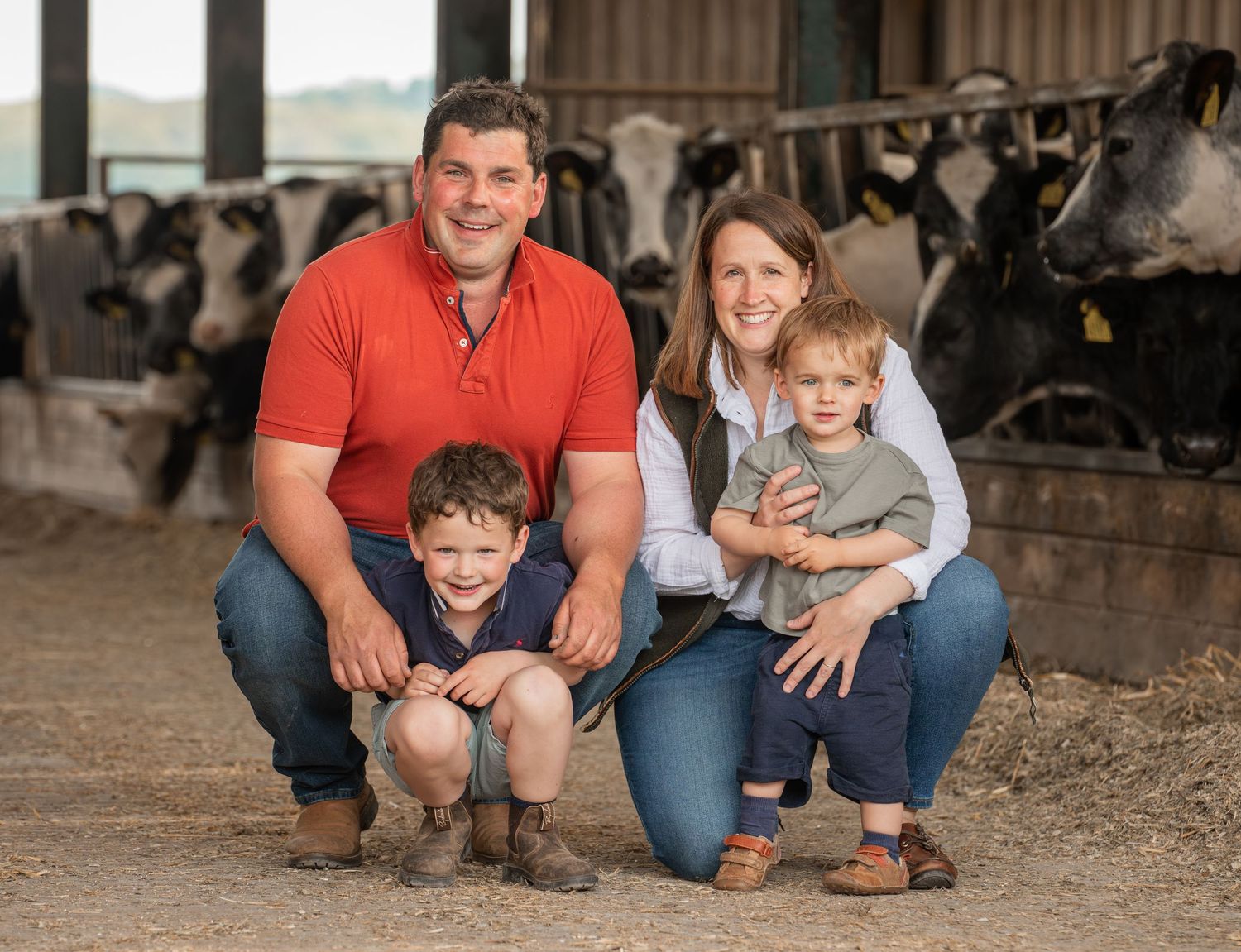 A family poses together in a rustic barn setting wearing coordinating red and blue outfits.