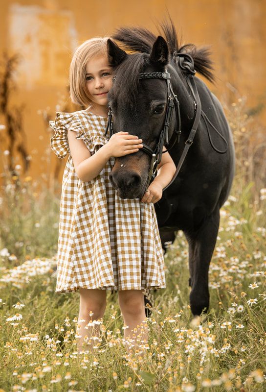 A black horse and someone in a checkered dress share a tender moment in a wildflower meadow during golden hour.