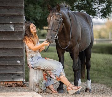 A rustic outdoor photo series featuring a woman in a white dress sitting near a brown horse in a pastoral setting.
