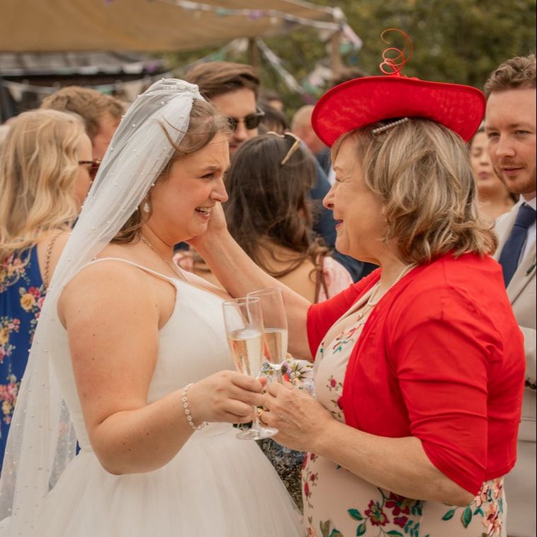 Wedding guests in red dresses gather around a bride in white during an outdoor celebration.