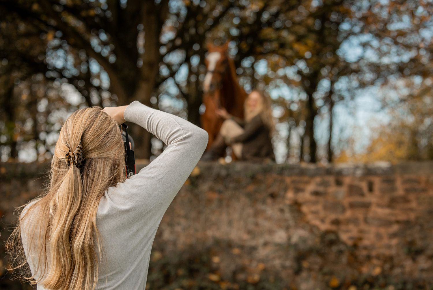 Photographer with long blonde hair taking pictures in an autumn forest setting.