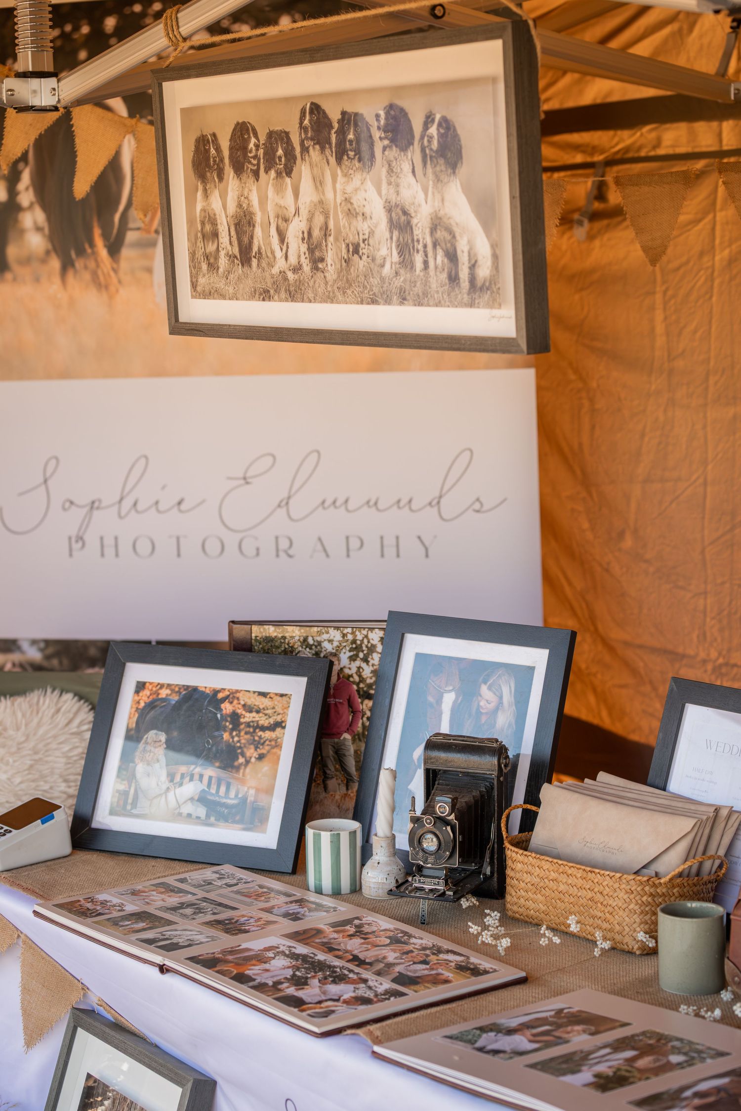 Sophie Edmunds Photography booth display with framed dog and portrait prints, vintage camera, and photo albums on a table.