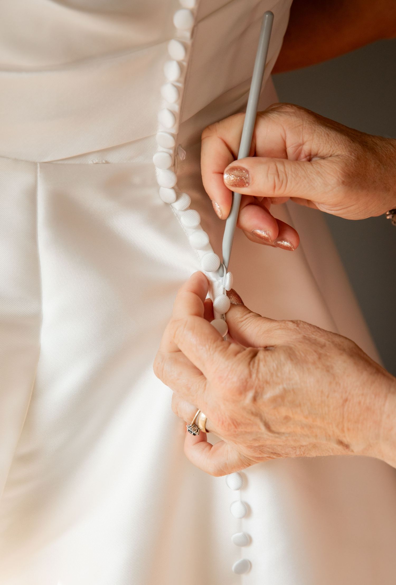 Close-up of hands fastening delicate pearl buttons on a white wedding dress.