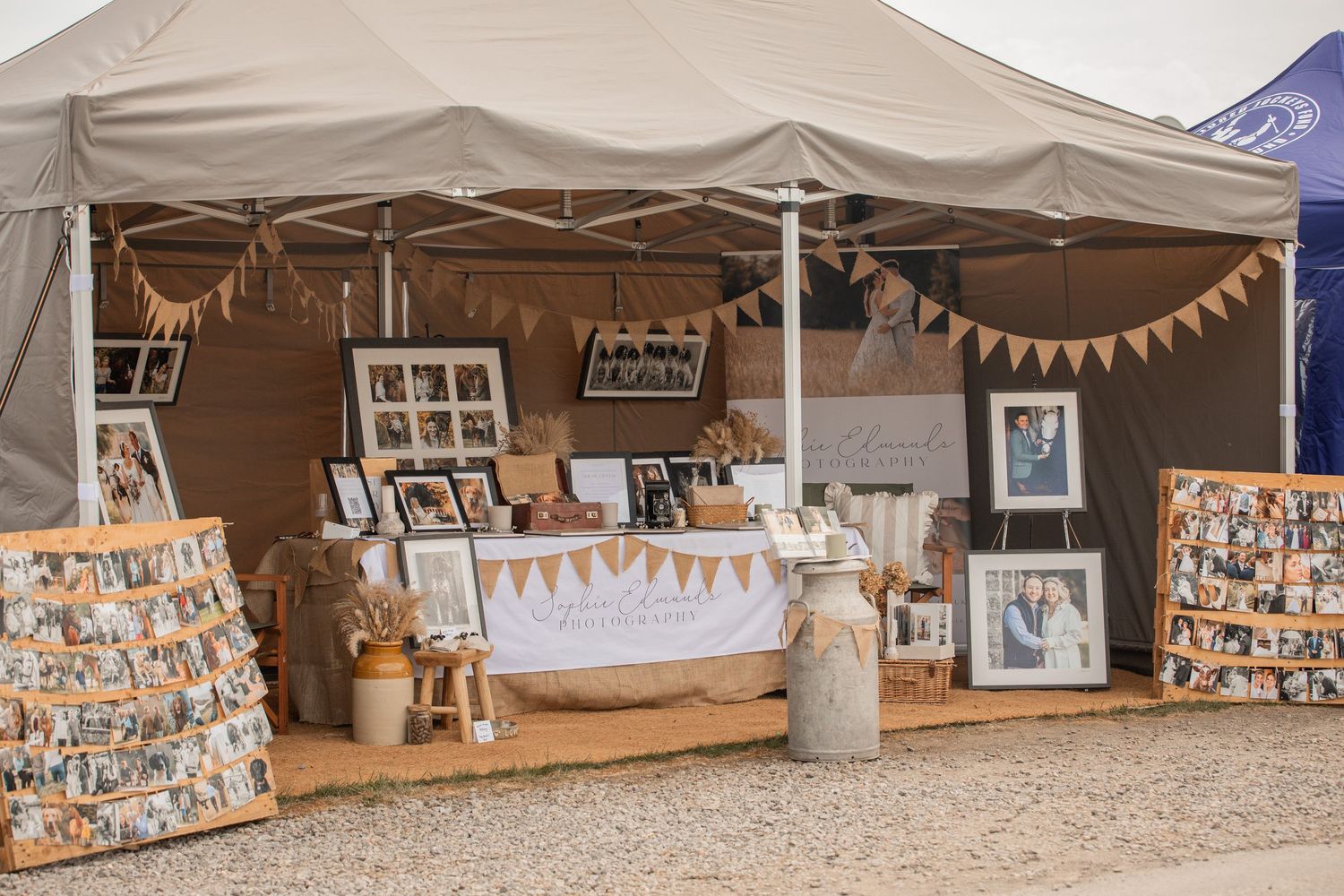 Rustic wedding photo display booth with framed pictures, bunting, and mason jars under a tent.