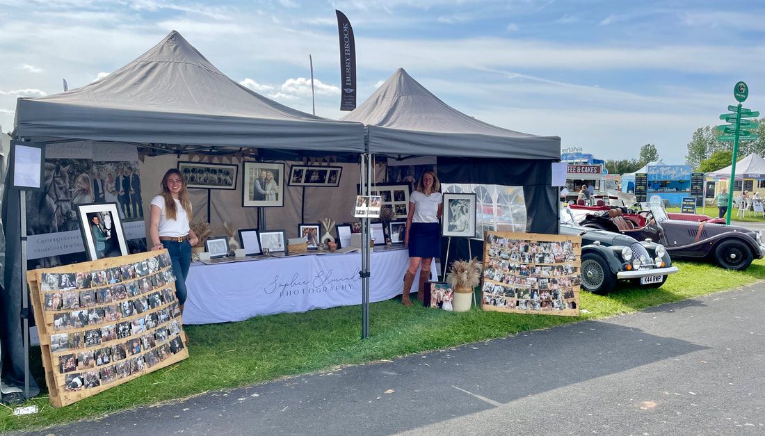 Outdoor vendor booth with pop-up tents displaying artwork and merchandise at a local market or fair.