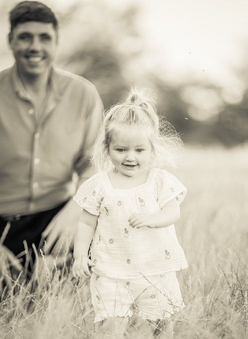 A series of vintage sepia photographs showing a small child in a white dress playing and laughing in tall grass.
