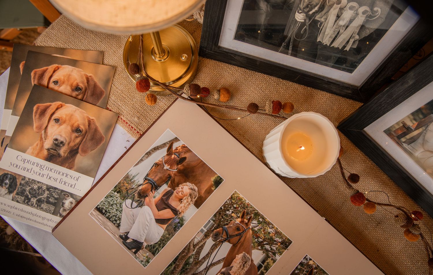A cozy table display with photo albums, framed pictures, a lit candle, and a dog portrait book arranged decoratively.