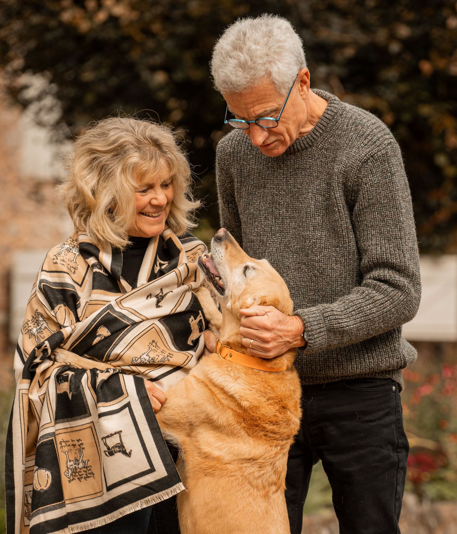 A couple and their golden retriever dog share a tender moment outdoors while looking at a photo album together.