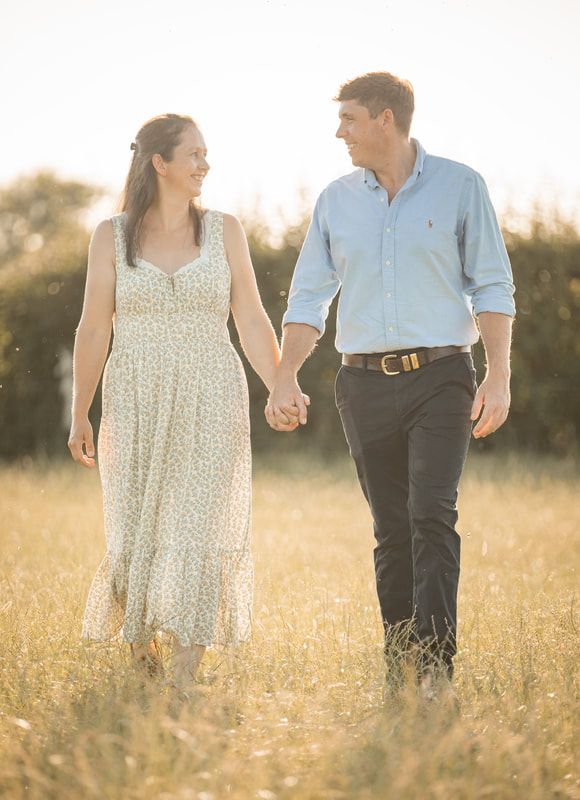 A couple walks hand in hand through a sunlit meadow of wildflowers during golden hour.
