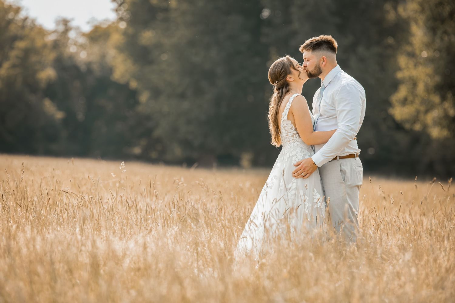 Romantic couple embracing in a sunlit field of tall grass.
