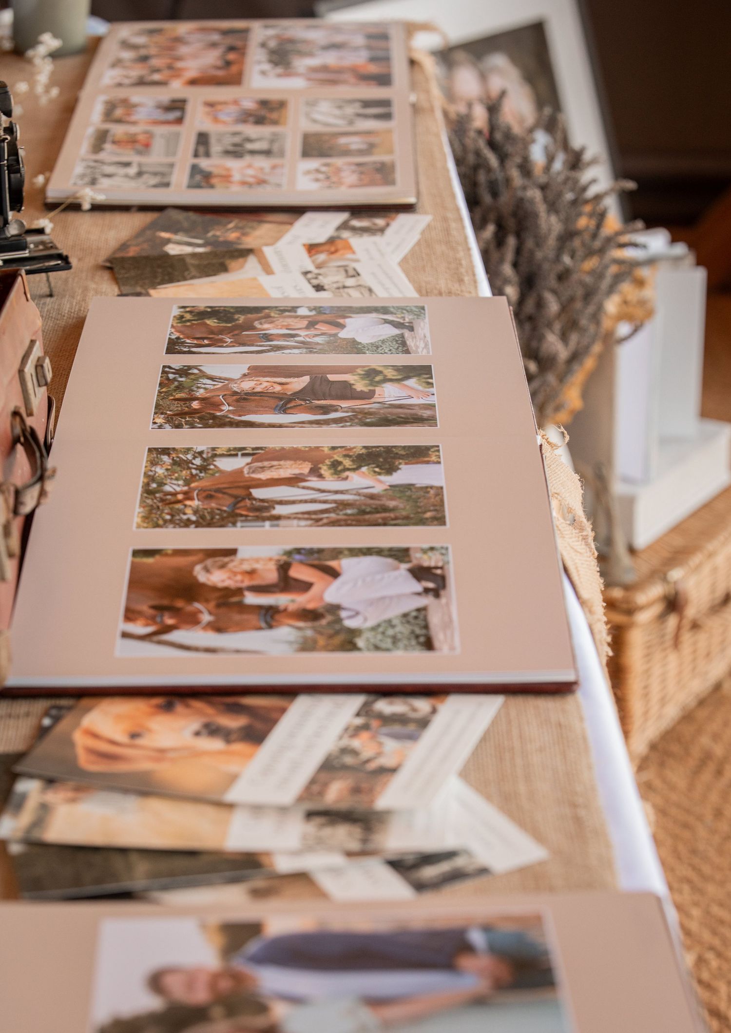 A display of printed photo albums and loose photographs arranged on a rustic wooden table at a photography showcase event.