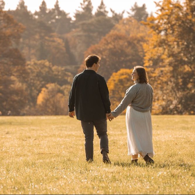 A couple walking together in a golden autumn field at sunset with warm sunlight illuminating the peaceful scene.