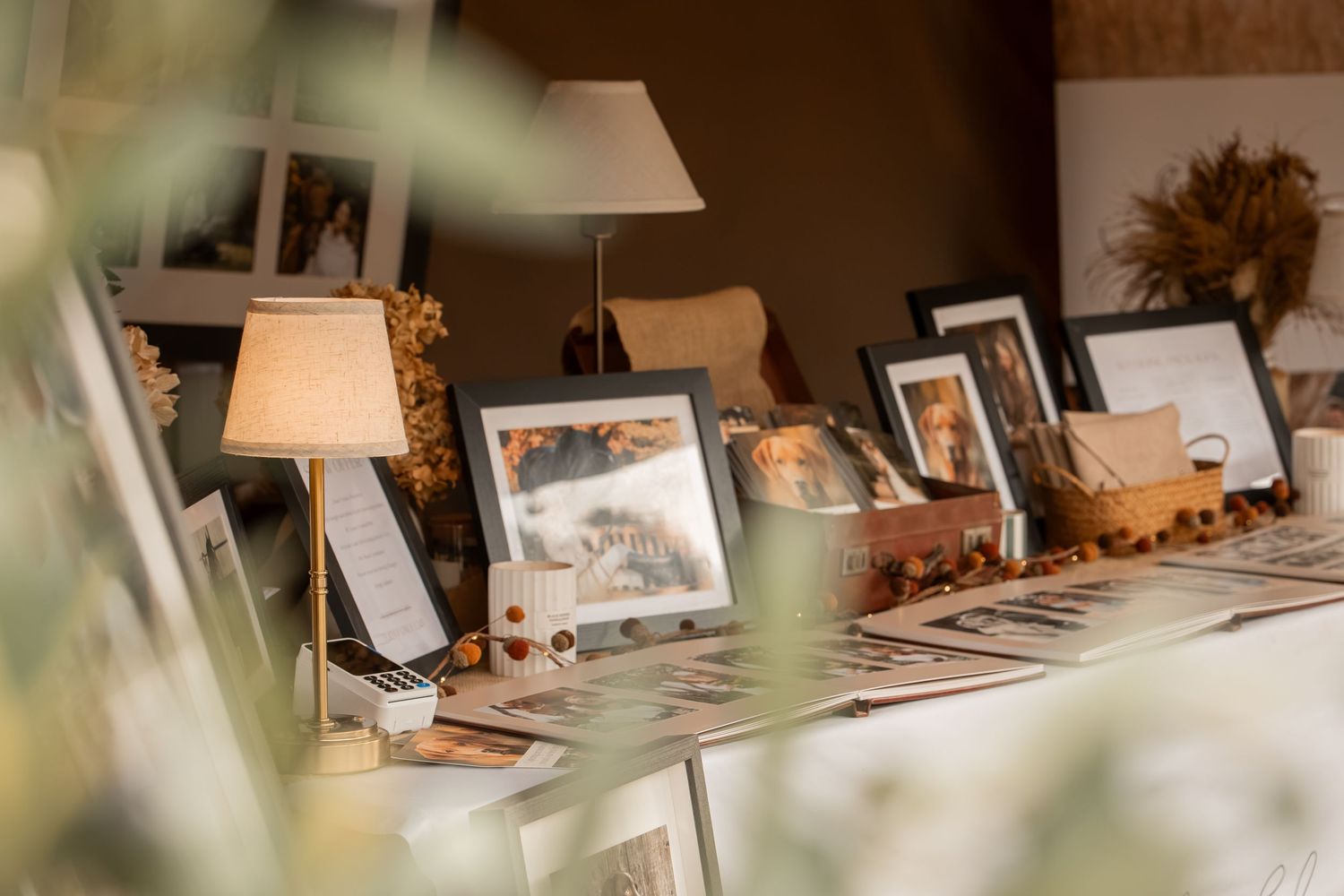 Elegant display of framed wedding photos on a table with a small lamp and dried floral decorations.