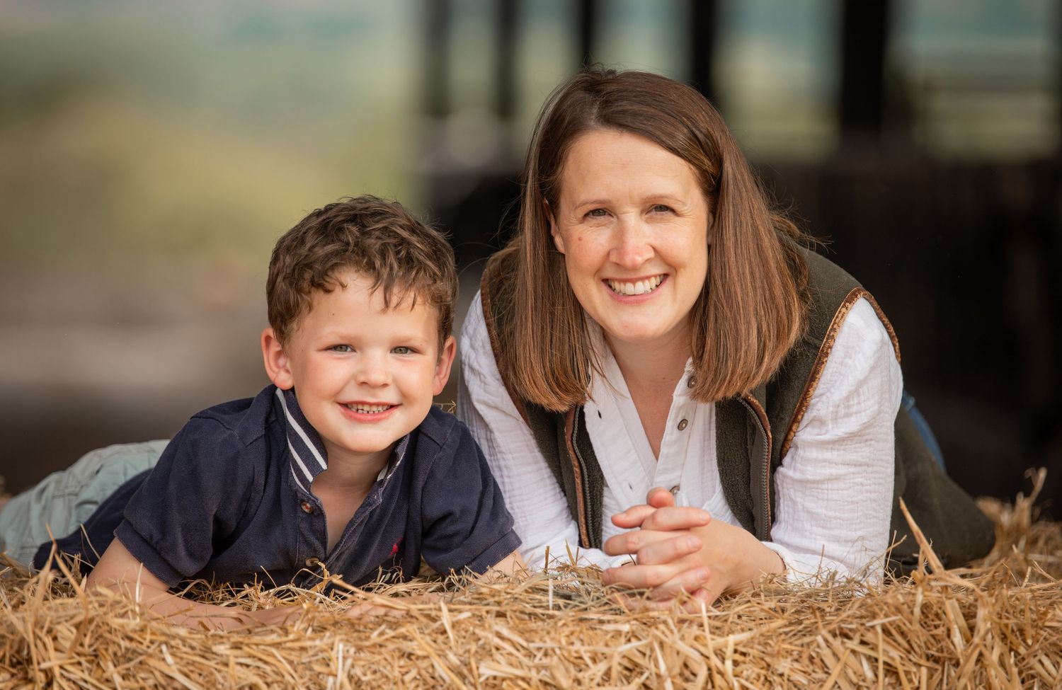 A family lies together in golden hay during an outdoor autumn photo session.