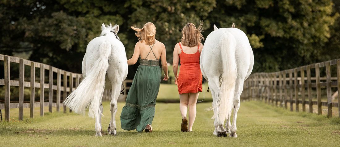 Group walking through a lush green field in elegant white and colored attire during a sunny day.