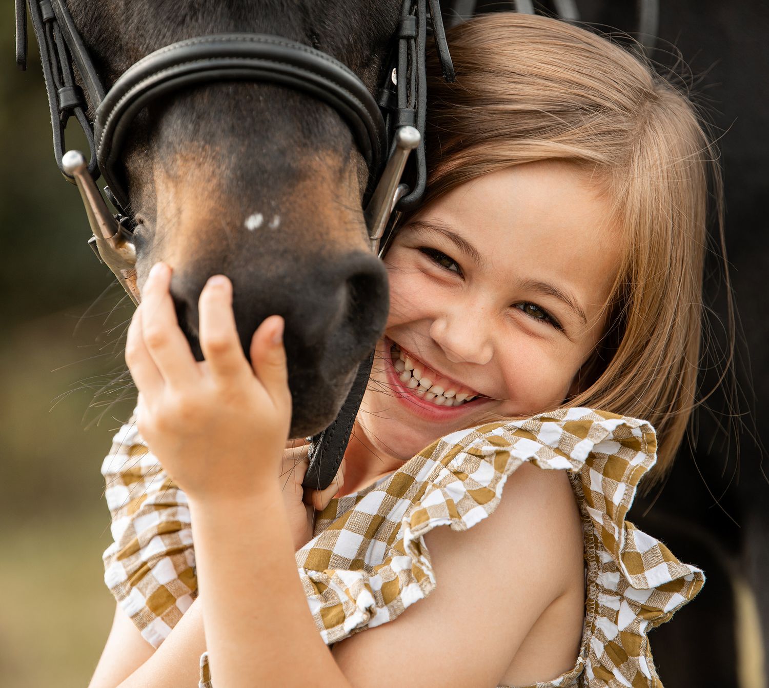 Tender moment between a little girl and dark horse wearing a gorgeous yellow gingham dress in summer during her equine photoshoot.
