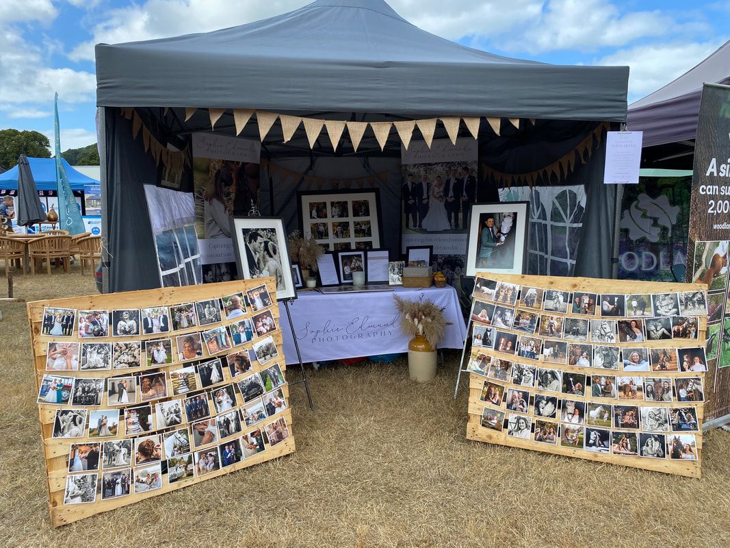 Photography vendor booth at an outdoor market with photo displays and bunting decorations.