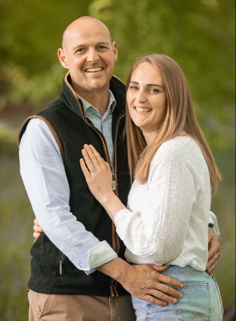 A couple poses together outdoors in coordinating outfits of white and black for engagement photos in a natural setting.