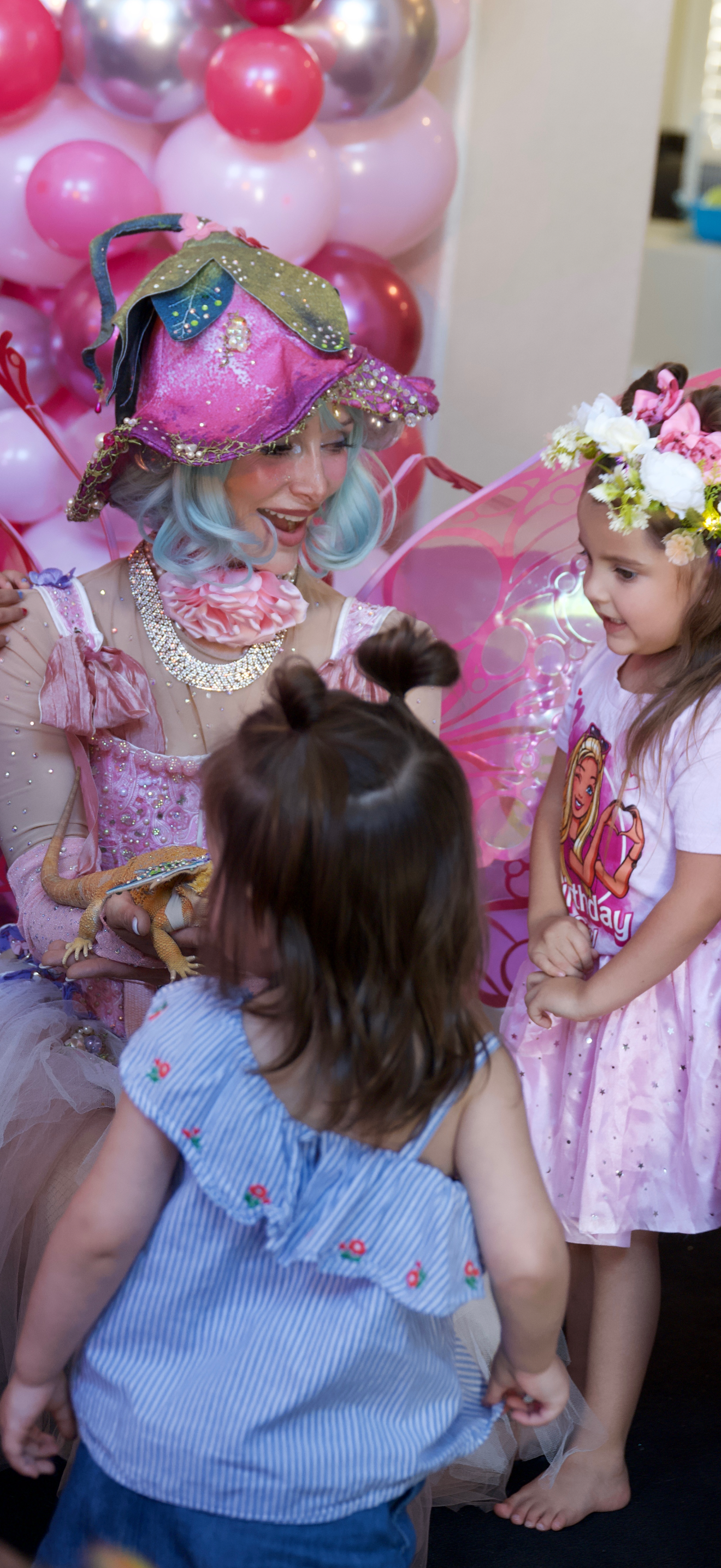 Party scene with pink balloon decorations and children in princess-themed costumes.