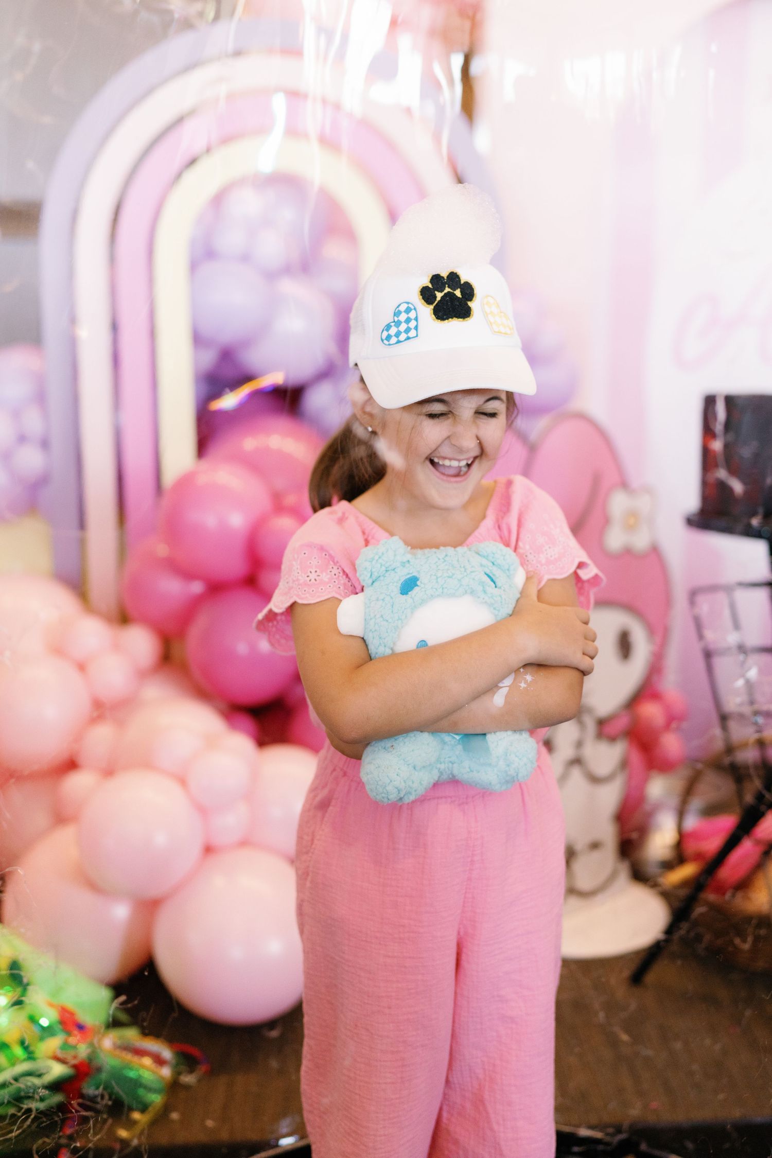 Children's party setup with pink decor and plush toys in pastel-colored environment.