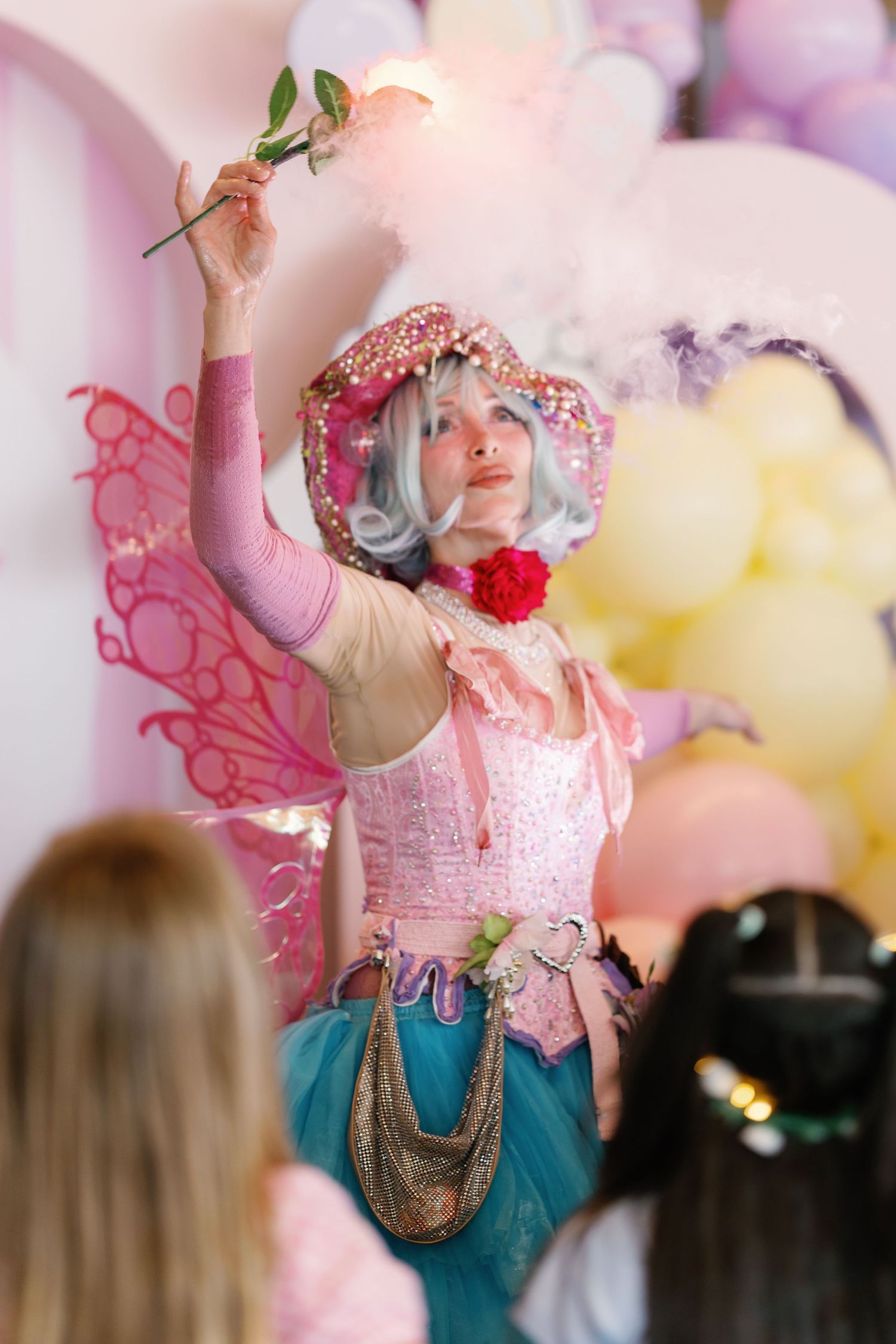 Entertainer in pink and turquoise costume performs energetically with dramatic gestures against blurred background.