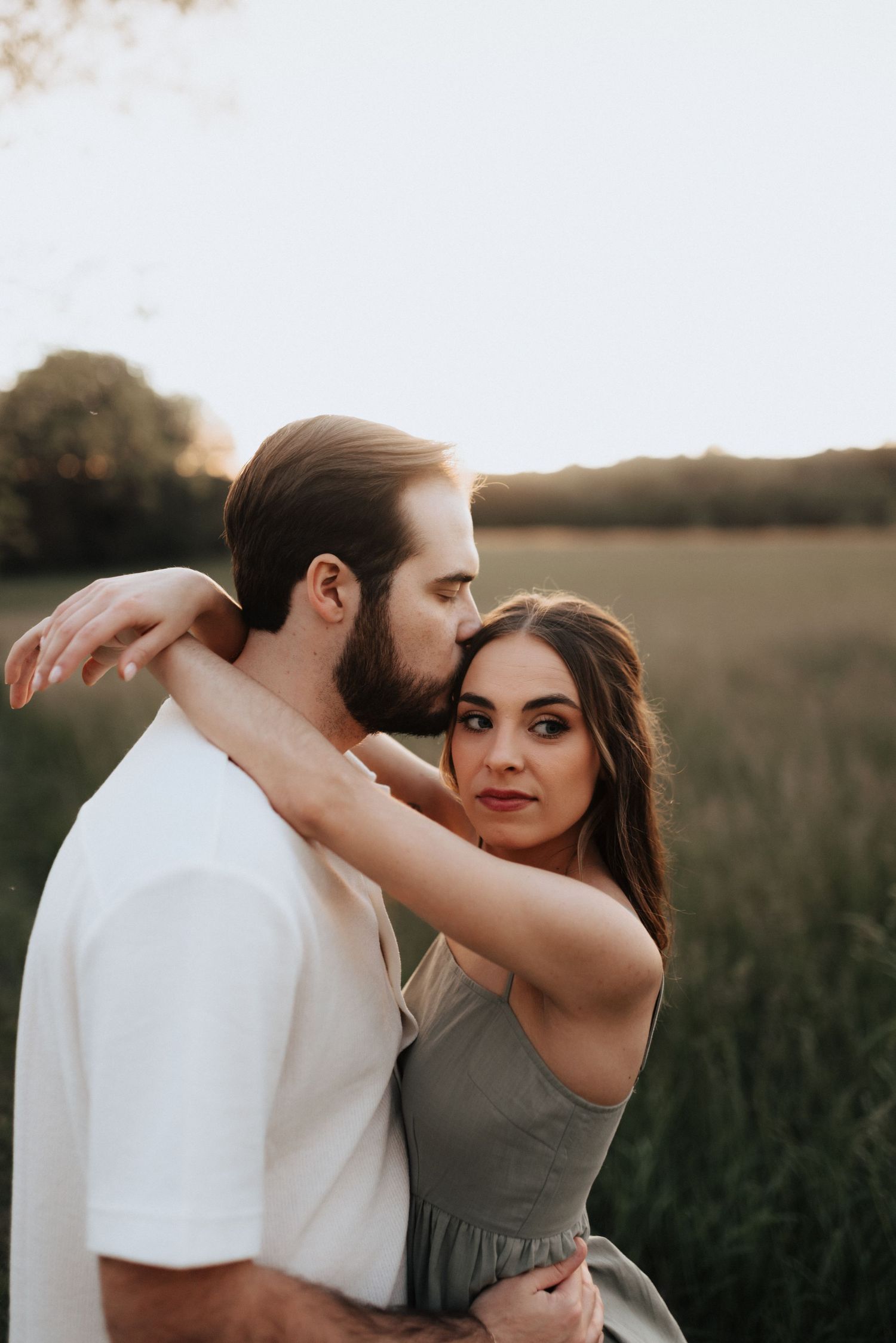 Romantic couple embracing in a golden field at sunset wearing white and gray.