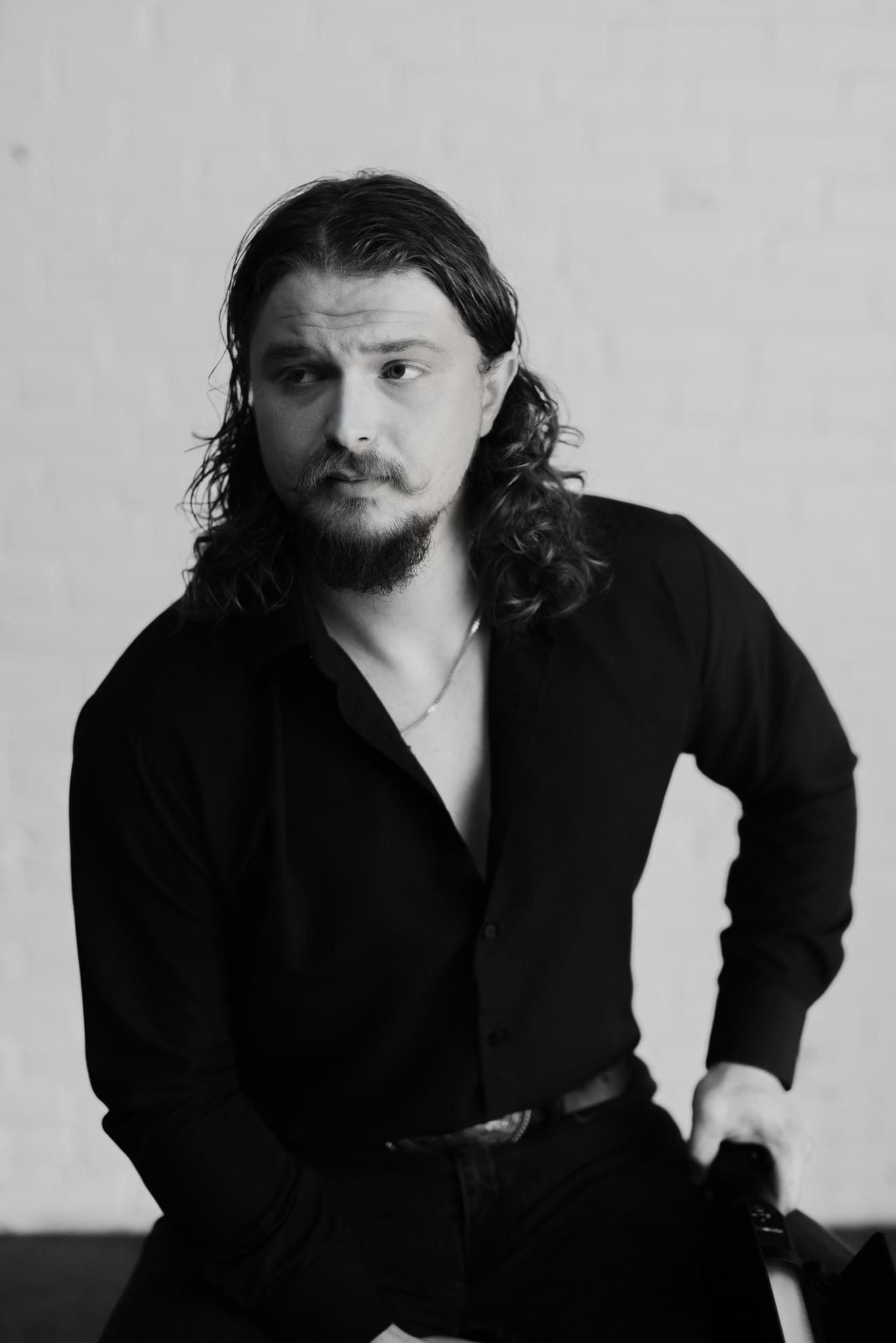 Black and white portrait of a man with long dark hair wearing a black shirt.