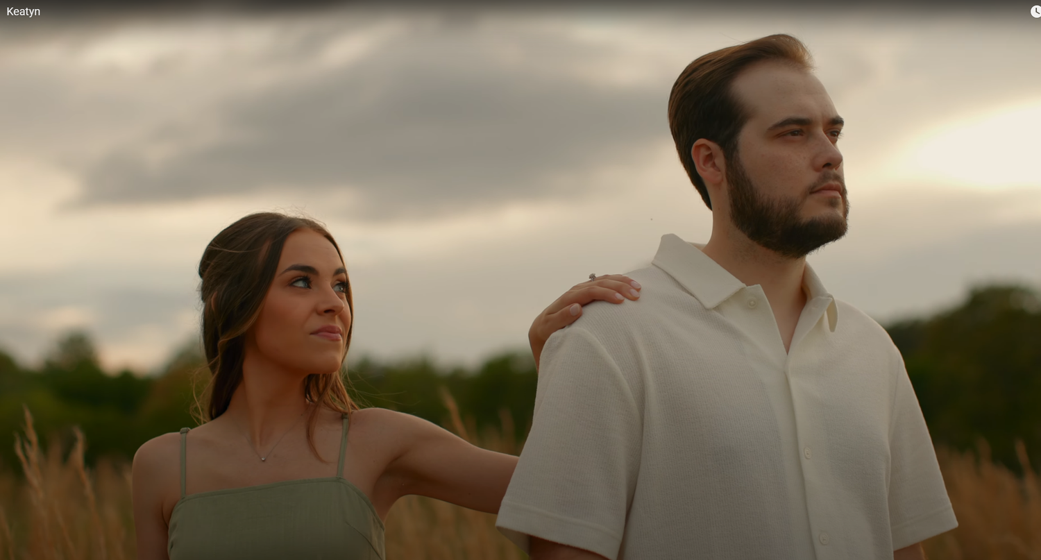 A couple standing together in a field during sunset.