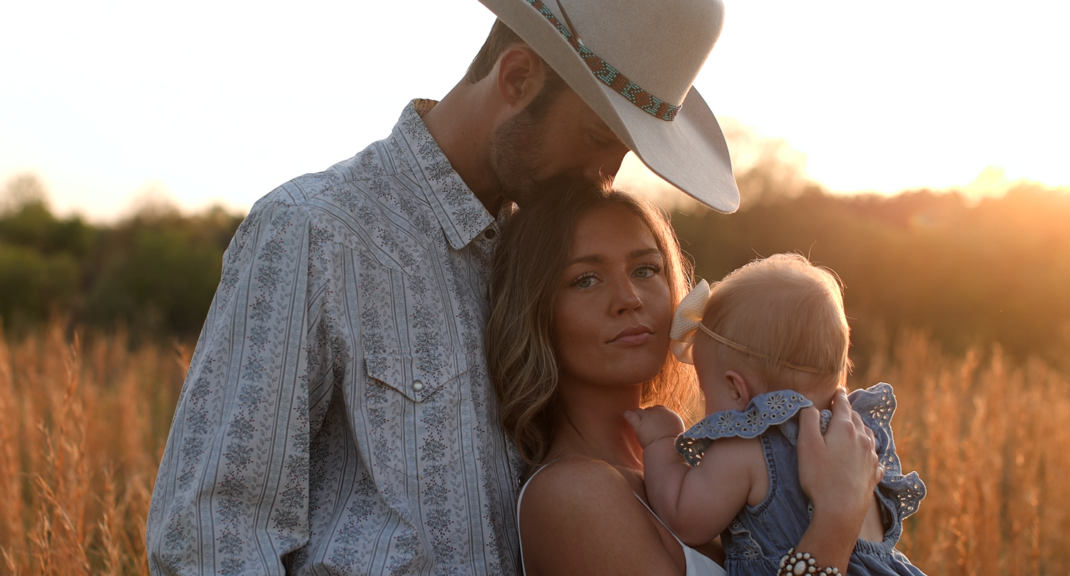 A family shares a tender moment in a sunlit field at golden hour.