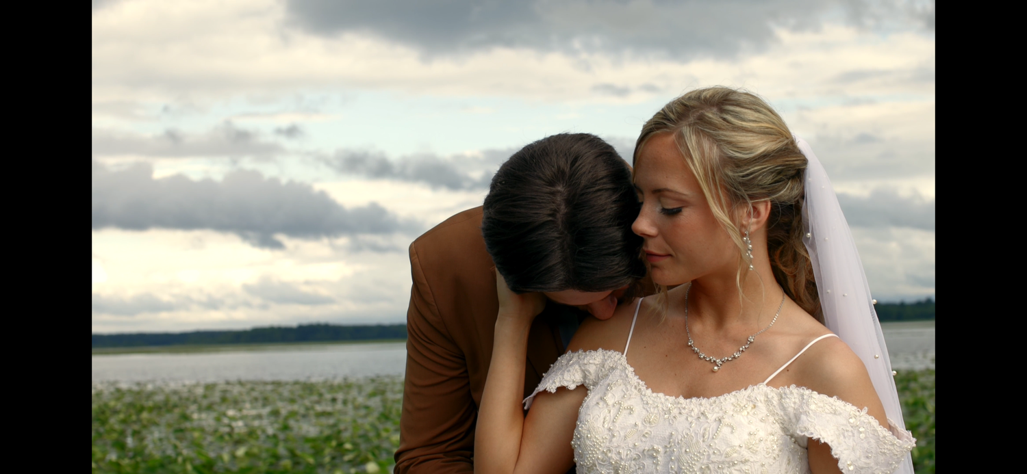 An intimate moment between a couple in a field with cloudy skies overhead.