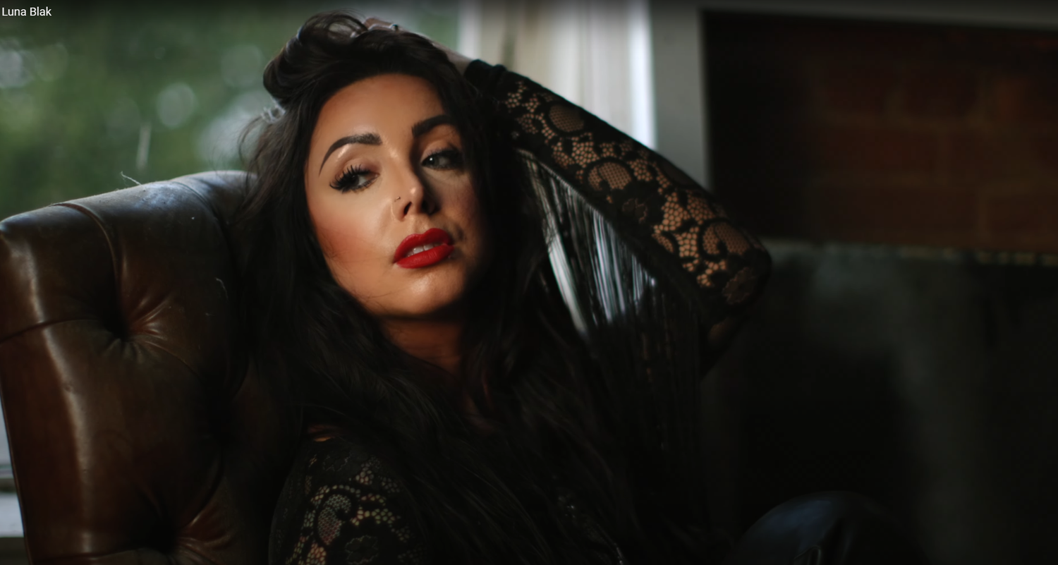 Woman in black lace lounging on leather chair with dramatic lighting and red lipstick.